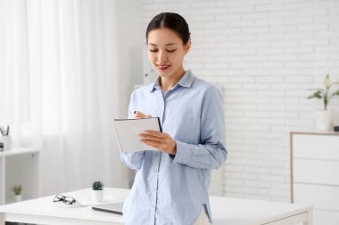 Not defteri olan genç Asyalı iş kadını ofiste çalışıyor.