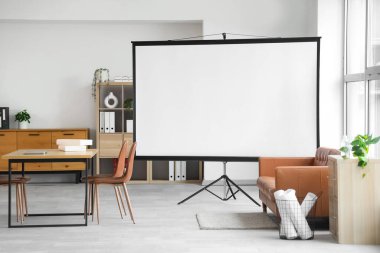 Konferans salonunun içinde projektör ekran, kanepe ve masa var.