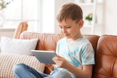 Modern tablet bilgisayarı olan sevimli küçük çocuk evdeki kanepede oturuyor.
