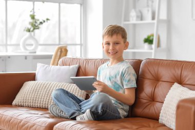 Modern tablet bilgisayarı olan sevimli küçük çocuk evdeki kanepede oturuyor.