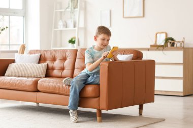 Evdeki koltukta oturan modern cep telefonlu şirin çocuk.