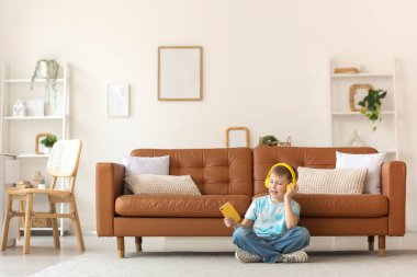 Modern cep telefonu ve kulaklığı olan sevimli küçük çocuk evde yerde oturuyor.