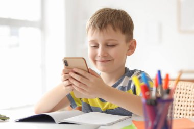 Modern cep telefonuyla evde ders çalışan şirin bir çocuk.