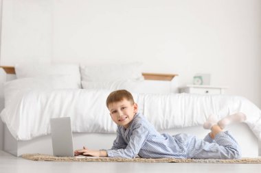 Modern dizüstü bilgisayarı olan şirin bir çocuk yatak odasında yerde yatıyor.