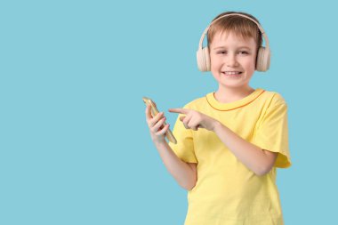 Kulaklıklı ve modern cep telefonlu şirin çocuk mavi arka planda müzik dinliyor.