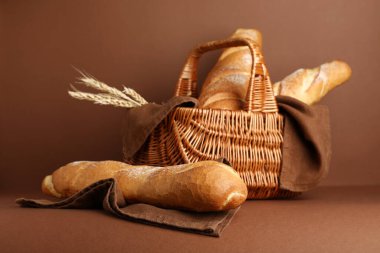 Hasır sepet, taze baget ve kahverengi arka planda buğday.