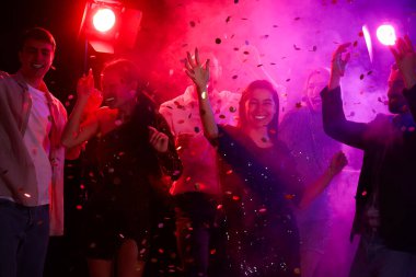 Bir grup genç gece kulübünde konfetiden düşüp dans ediyor.