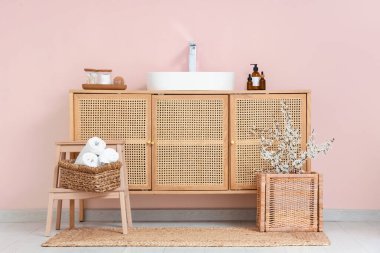 Lavabonun içinde sepetin içinde dallar ve çekmecelerin göğüs kısmında pembe duvarın yanında lavabo var.