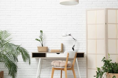 Modern çalışma alanı, katlanan ekran ve hasır sepetlerde ev bitkileri olan şık bir oda.