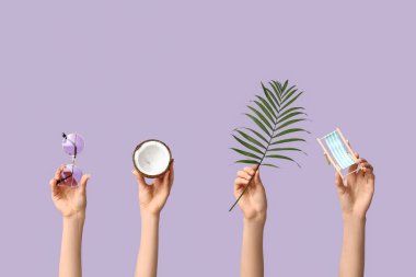 Palmiye yaprağı, hindistan cevizi ve leylak arkaplanda güneş gözlüğü olan mini güverte sandalyesi tutan kadın eller.