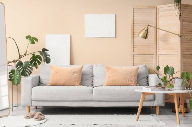 Masa, kanepe ve evin çiçekleri odanın içindeki bej duvarın yanında.