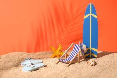 Kumlu yaz kompozisyonu, dekoratif sörf tahtası, parmak arası terlikler, kırmızı arka planda iskemle ve şapka, yakın plan.