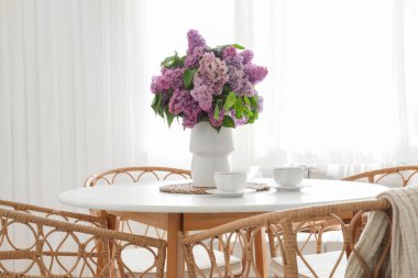 Odadaki yemek masasında leylak çiçekli vazo ve çay.