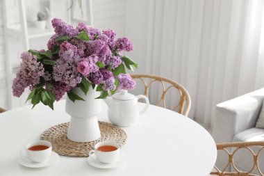 Odadaki yemek masasında leylak çiçekli vazo ve çay.
