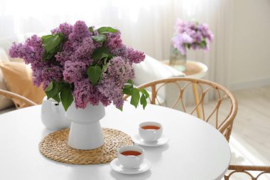 Odadaki yemek masasında leylak çiçekli vazo ve çay.