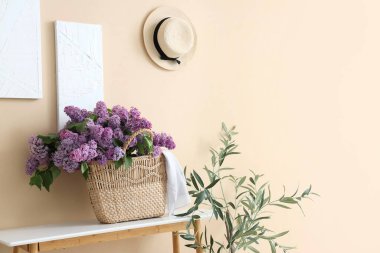 Odadaki bej duvarın yanındaki masada leylak çiçekli hasır çanta.