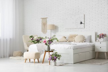 Rahat yatağı ve güzel çiçekleri olan aydınlık yatak odasının içi.