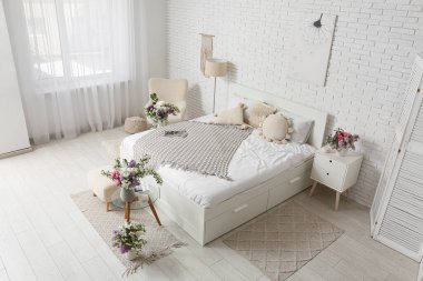 Rahat yatağı ve güzel çiçekleri olan aydınlık yatak odasının içi.