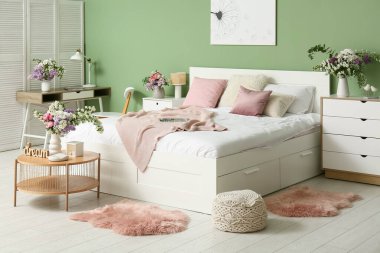 Rahat yatağı, masası ve güzel çiçekleri olan şık bir yatak odası.