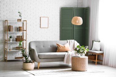 Oturma odasının içinde çiçek açan leylak dalları olan kanepe ve hasır sehpa.