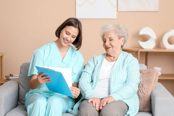 Молодая медсестра с планшетом и пожилая женщина сидит на диване дома