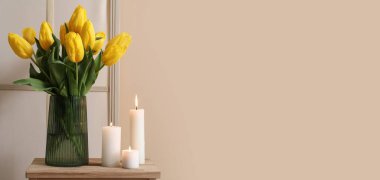 Bej duvarın yanındaki masada mum ve vazoda çiçekler yakmak. Tasarım için pankart