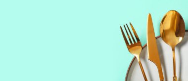 Turkuaz arka planda altın çatal bıçak seti olan güzel bir masa.