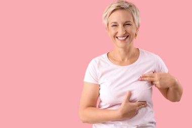 Güzel olgun bir kadın pembe arka planda göğüslerini kontrol ediyor. Kanser farkındalığı kavramı