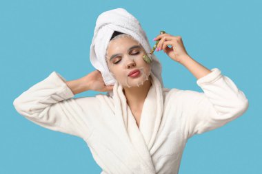 Bornozlu genç bir kadın, maske takıyor. Masaj maskesini arka planda kullanıyor.