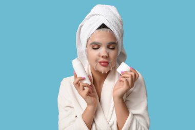 Bornozlu, çarşaf maskeli, renkli arka planda kozmetik ürünler taşıyan güzel bir kadın.