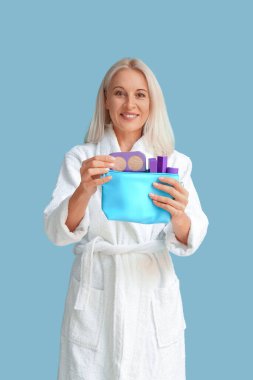 Bornoz giymiş olgun bir kadın. Elinde makyaj malzemesi olan bir çanta var.