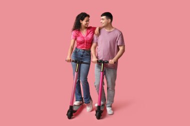 Pembe arka planda modern elektrikli scooterları olan güzel genç bir çift.