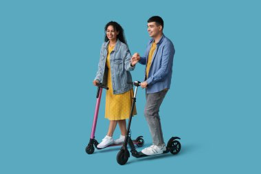 Mavi arka planda modern elektrikli scooter kullanan güzel bir çift.