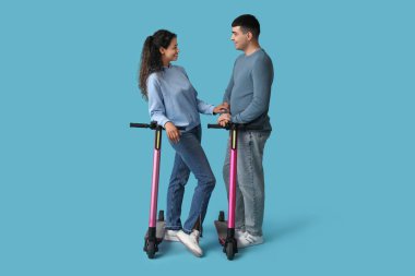 Mavi arka planda modern elektrikli scooterları olan güzel genç bir çift.