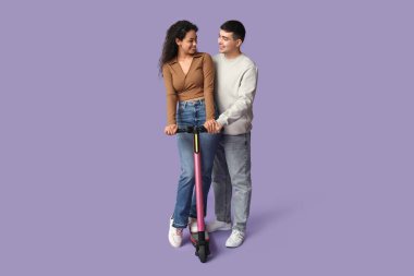 Mor arka planda modern elektrikli scooterı olan güzel genç bir çift.