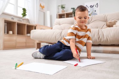 Evinde yerde keçeli kalemlerle çizen sevimli küçük çocuk.