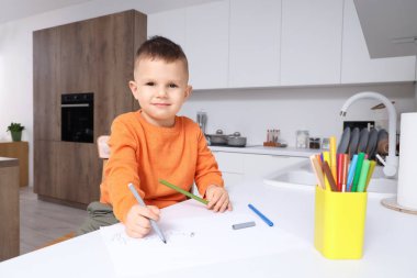 Mutfaktaki masada keçeli kalemlerle resim yapan küçük çocuk.