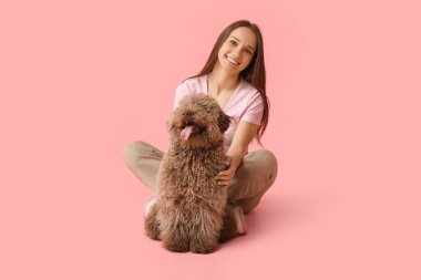 Kahverengi köpekli genç bir kadın pembe arka planda oturuyor.