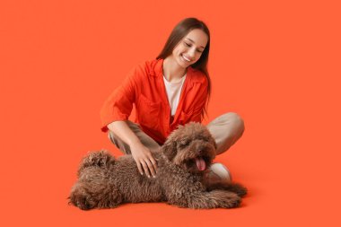 Kırmızı arka planda oturan sevimli kahverengi kaniş köpekli genç bir kadın.