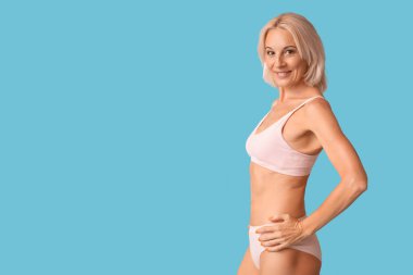 Güzel, olgun, mutlu, mavi arka planda iç çamaşırlı, pozitif kadın.