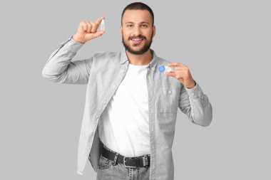 Gri arka planda göz damlası ve kontakt lens tutan genç adam.