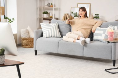 Genç kadın evde kanepede televizyon izlerken