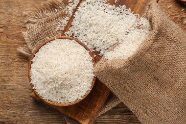 Tahta arka planda çiğ pirinç dolu kase ve çuval.