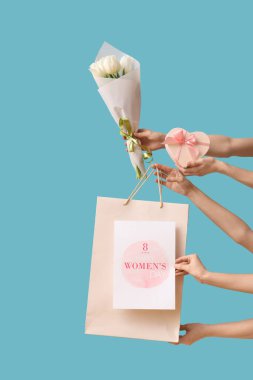 Çiçekleri hediye kutusu, kartpostal ve mavi arka planda kese kağıdı olan kadın eller. Uluslararası Kadınlar Günü için Alışveriş