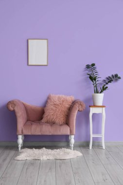 Mor duvarın yanındaki taburede şık bir kanepe ve çiçek var.