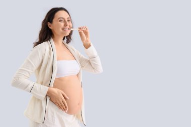 Dişlerini arka planda fırçalayan hamile bir kadın.