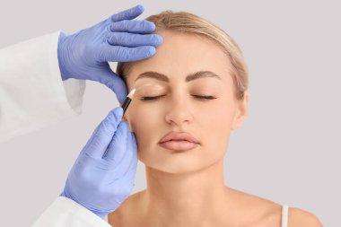 Plastik cerrah kadının yüzünü arka plandaki ışığa göre işaretliyor, yakın plan. Blepharoplasty konsepti