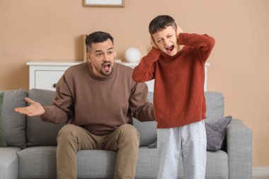 Baba ve oğlu evde ağız dalaşı yaparken kulaklarını kapatıyorlar.