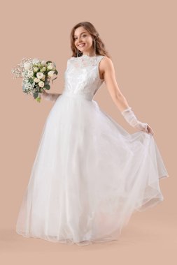 Bej arkaplanda çiçekler olan beyaz gelinlik içinde güzel bir gelin.