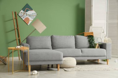 Gri kanepeli dağınık oturma odasının içi, standart lambayı ters çevirmiş ve depremden sonra etrafa saçılmış eşyalar.